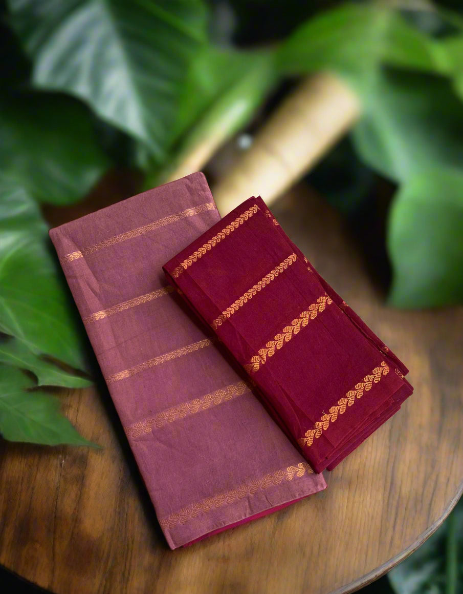 Two folded sarees in purple and red with gold patterns on a woven mat.
