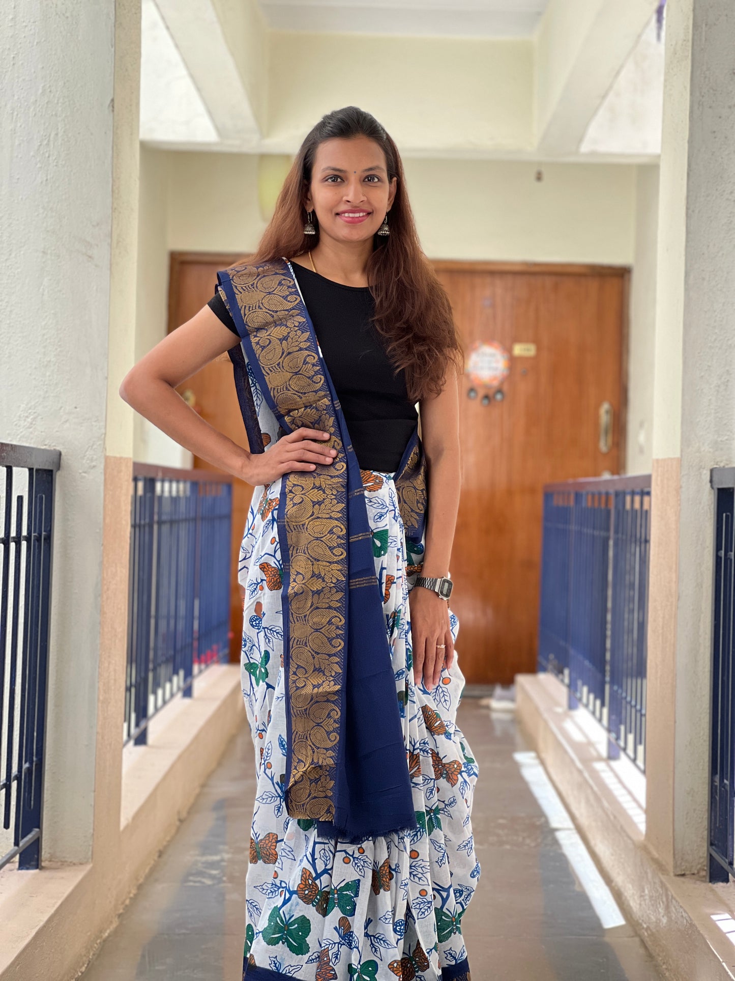 Woman in a floral Saree with a long scarf standing in a hallway.