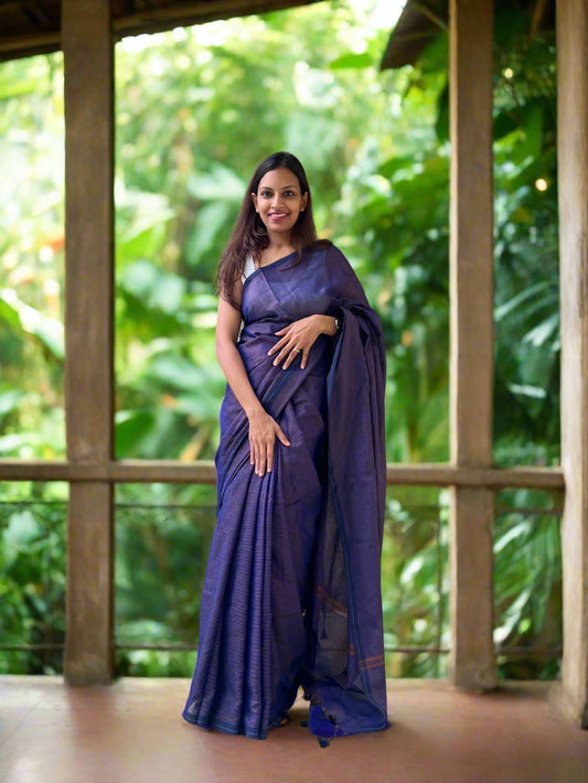 Woman in a purple saree standing on a balcony with stone wall and greenery in the background