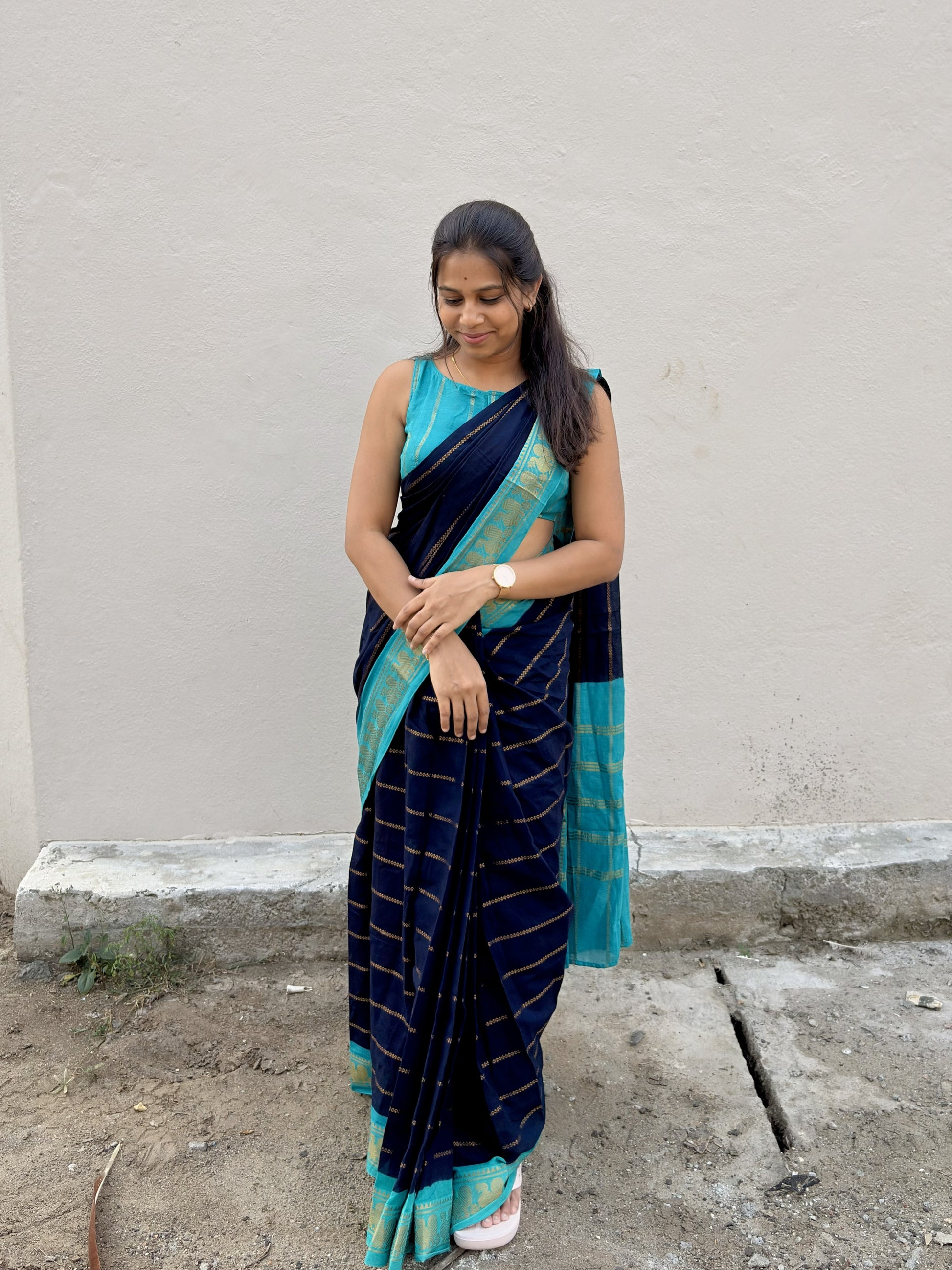 Woman wearing a blue and blue saree against a plain wall.