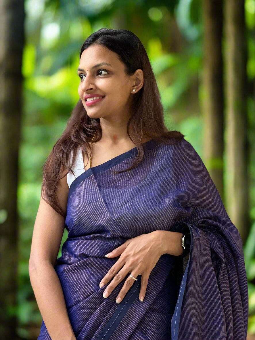 Woman wearing a blue saree standing against a stone wall.
