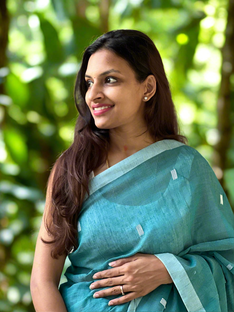 Woman in a teal saree standing against a stone wall