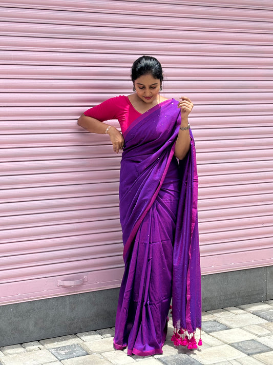 Woman wearing a purple saree with a pink blouse against a pink shutter background