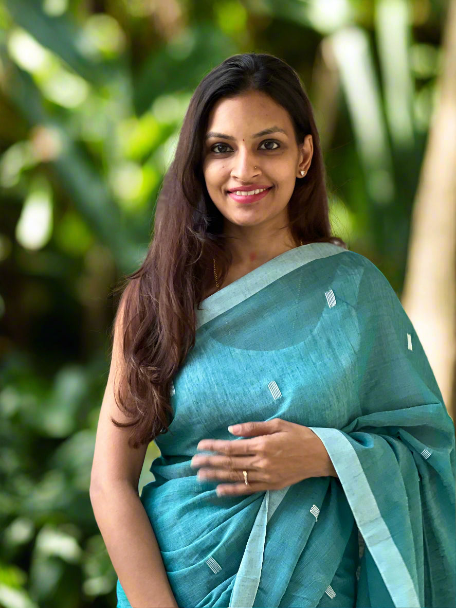 Woman in a teal saree standing against a stone wall