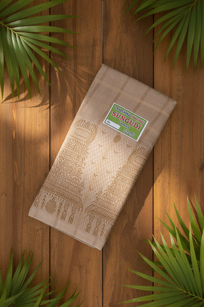 A folded beige cotton saree with brown printed patterns and a green 'Sungudi' brand label, displayed on a woven straw mat.