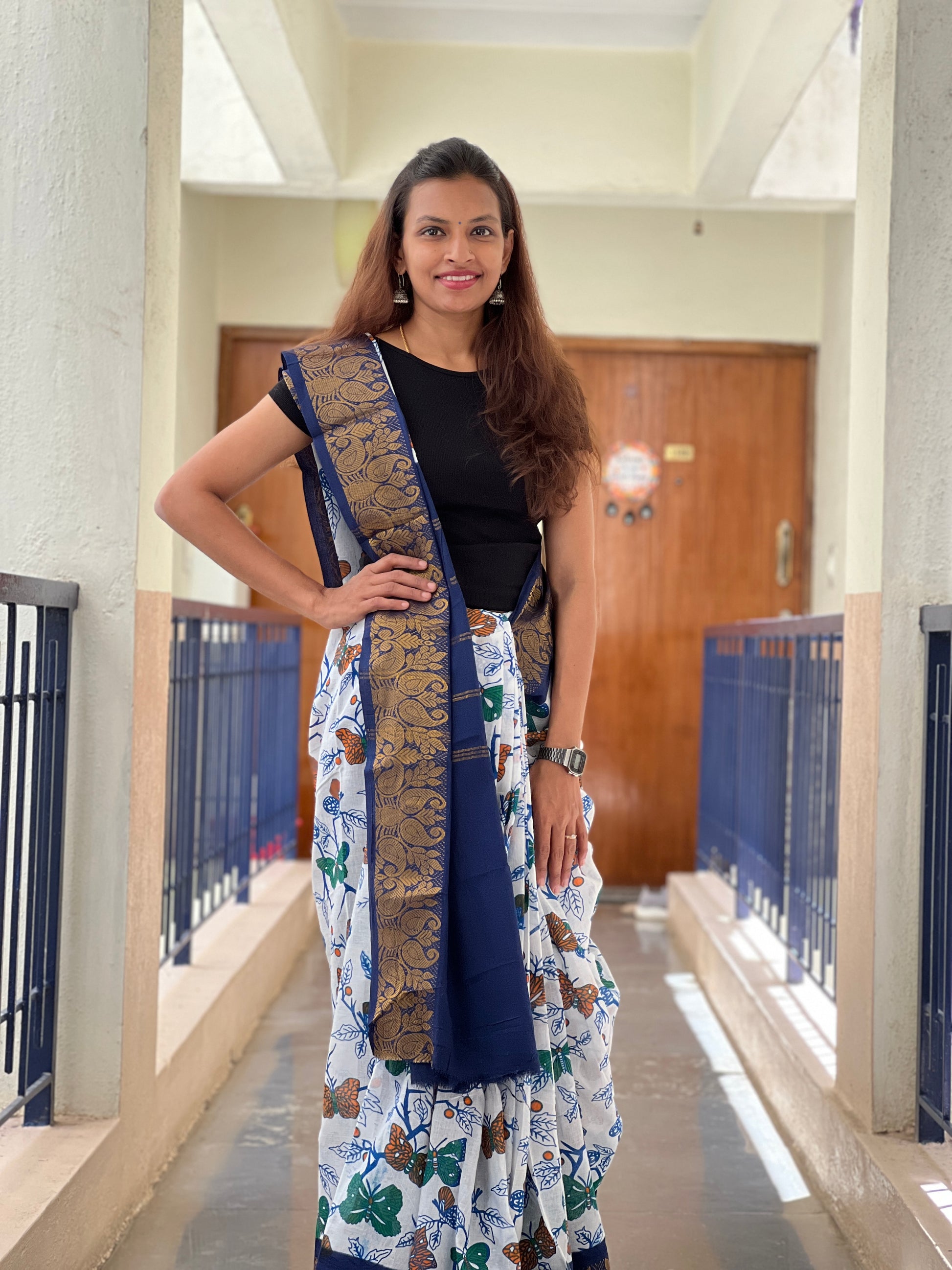 Woman in a floral Saree with a long scarf standing in a hallway.