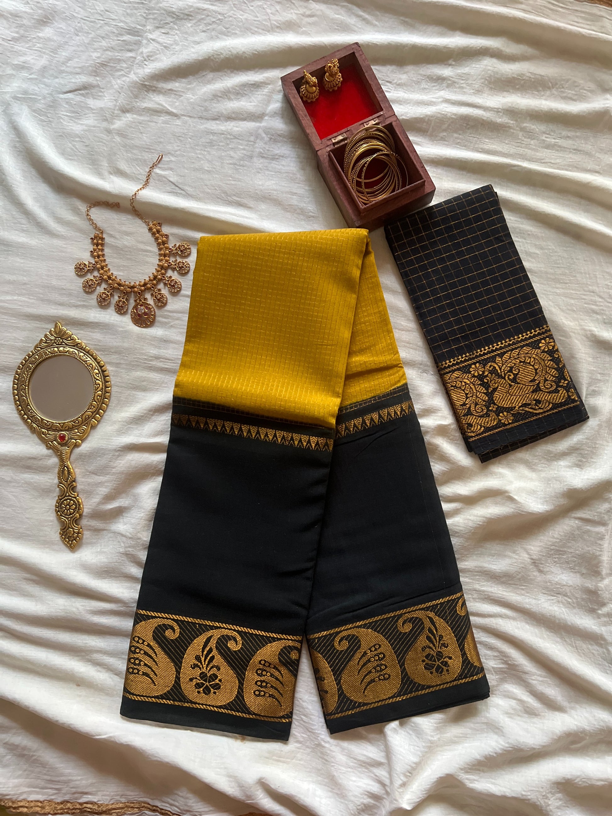 Black and yellow traditional saree with jewelry on a white fabric background