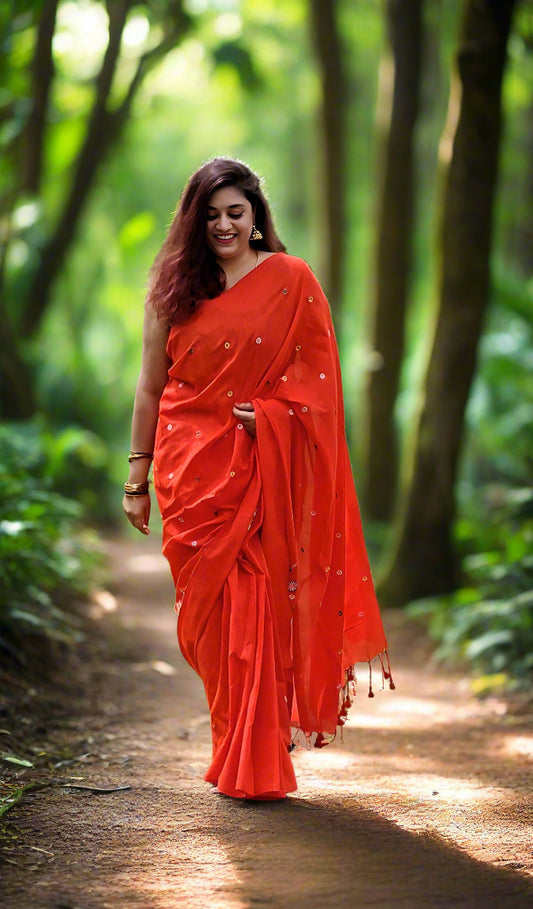 Woman in a bright orange saree standing in a grassy field with trees in the background