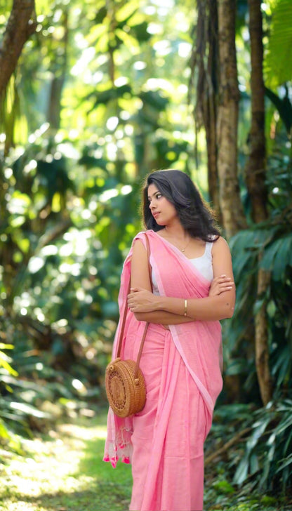 Woman in a pink saree standing outdoors with greenery in the background