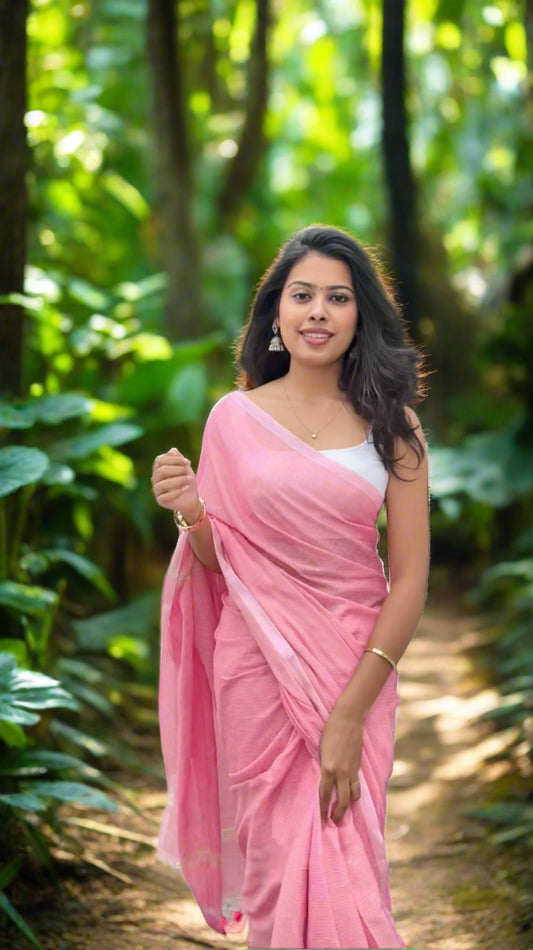 Woman in a pink saree standing outdoors with greenery in the background