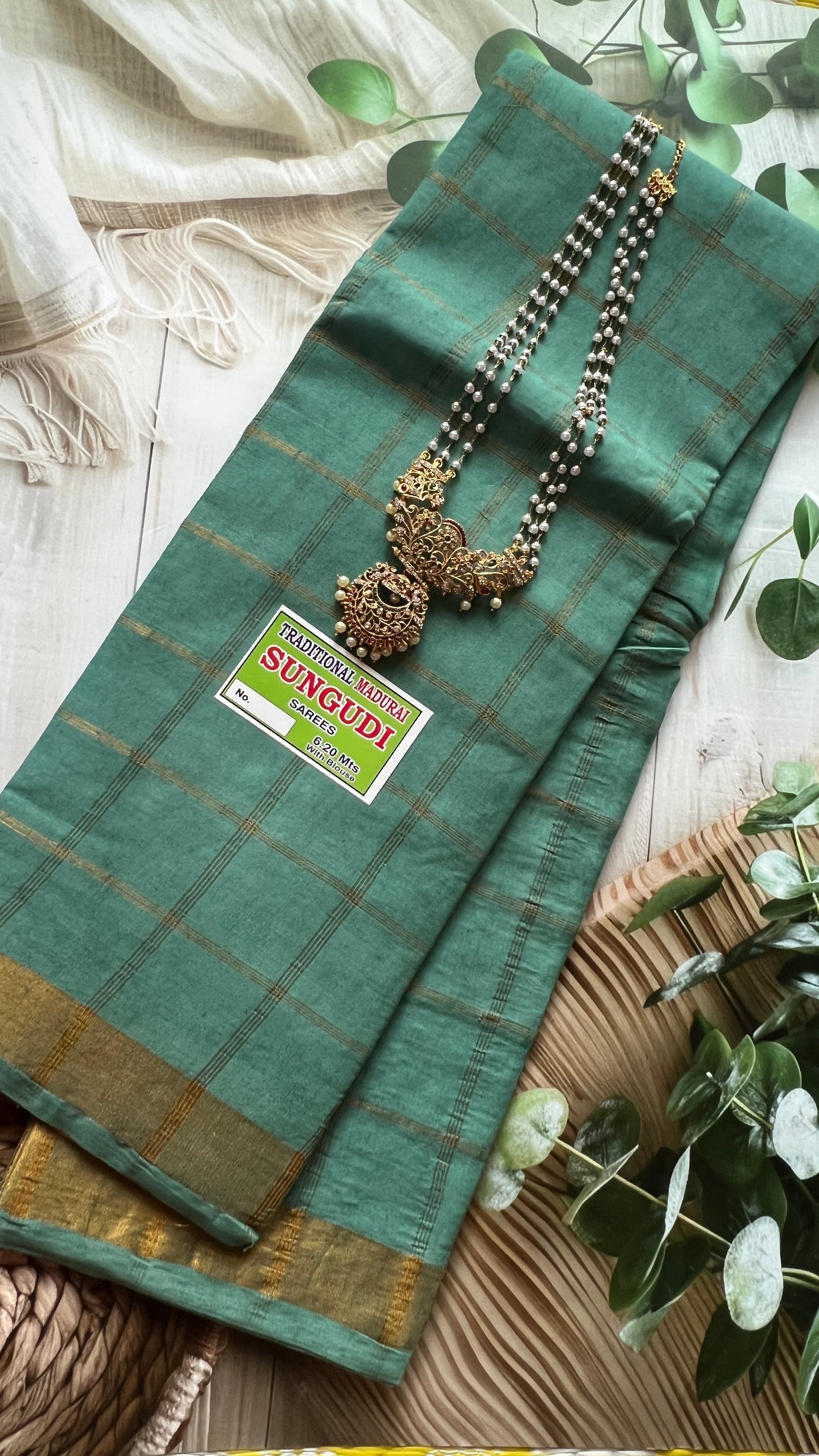 Green saree with gold border and necklace on a wooden surface with greenery