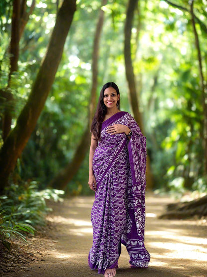 Woman in a purple saree standing on a balcony with a stone wall and trees in the background